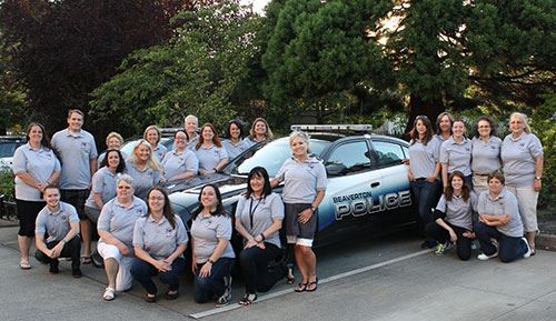 Blue shirted victim advocates group photo in front of Beaverton police vehicle.